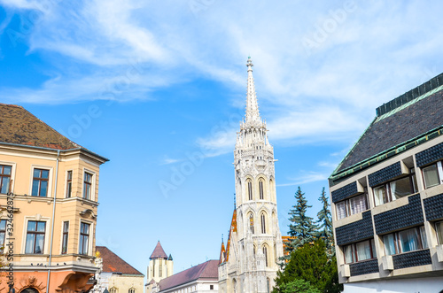 Spire of the Matthias Church in Budapest, Hungary on a horizontal photo with adjacent Socialist building. Roman Catholic church built in the Gothic style. Blue sky and white clouds. Eastern Europe © ppohudka