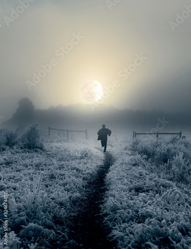 Dramatic artistic image of man running toward rising moon in winter landscape