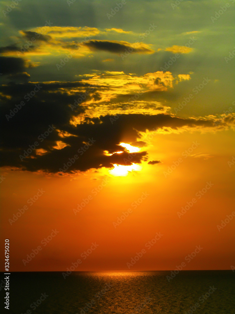 Fototapeta premium The sun hid behind the clouds at sunset over the sea