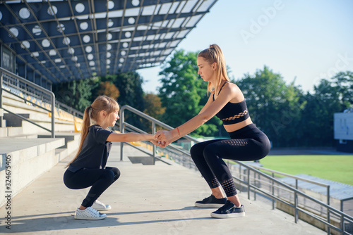 Sporty beautiful elder and younger sisters which squating together during fitness training outdoors. photo