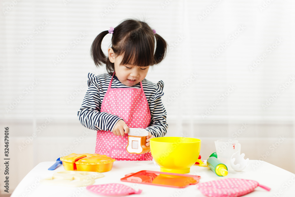 toddler girl pretend play food preparing role at home agianst white background