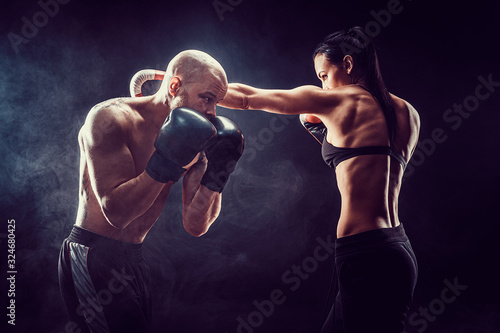 Shirtless Woman exercising with trainer at boxing and self defense lesson, studio, smoke on background. Female and male fight,