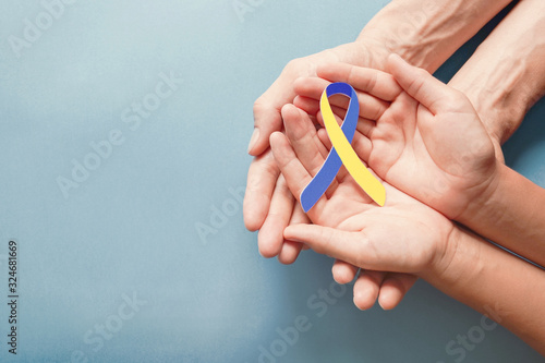 Adult and child hands holding blue and yellow ribbon shaped paper, Down syndrome awareness , World down syndrome day photo