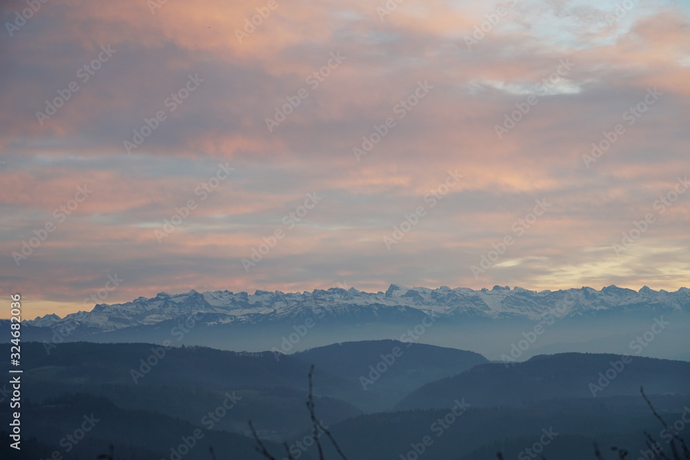 Sunset panorama of Alps over canton Zurich, Switzerland. The whole landscape is veiled in fog. The sky is colorful at sunset. 