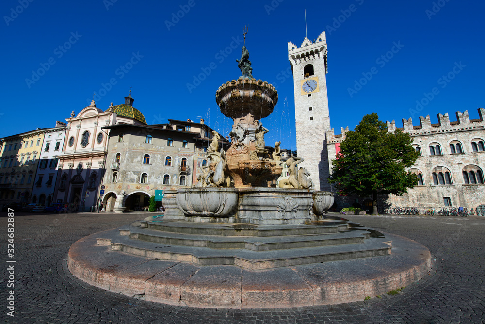 Fontana con scalini e statue che fuoriesce acqua del centro città di Trento, con sfondo delle case residenziali e della chiesa