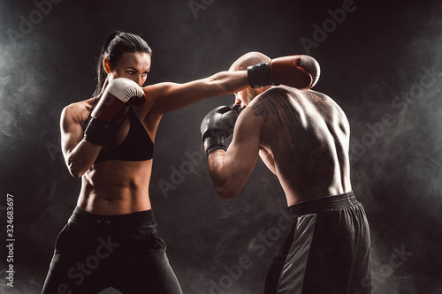 Foto Woman exercising with trainer at boxing and self defense lesson, studio, smoke on background