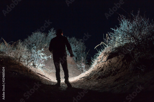 Man explores dark landscape at night using flashlight, artistic photo