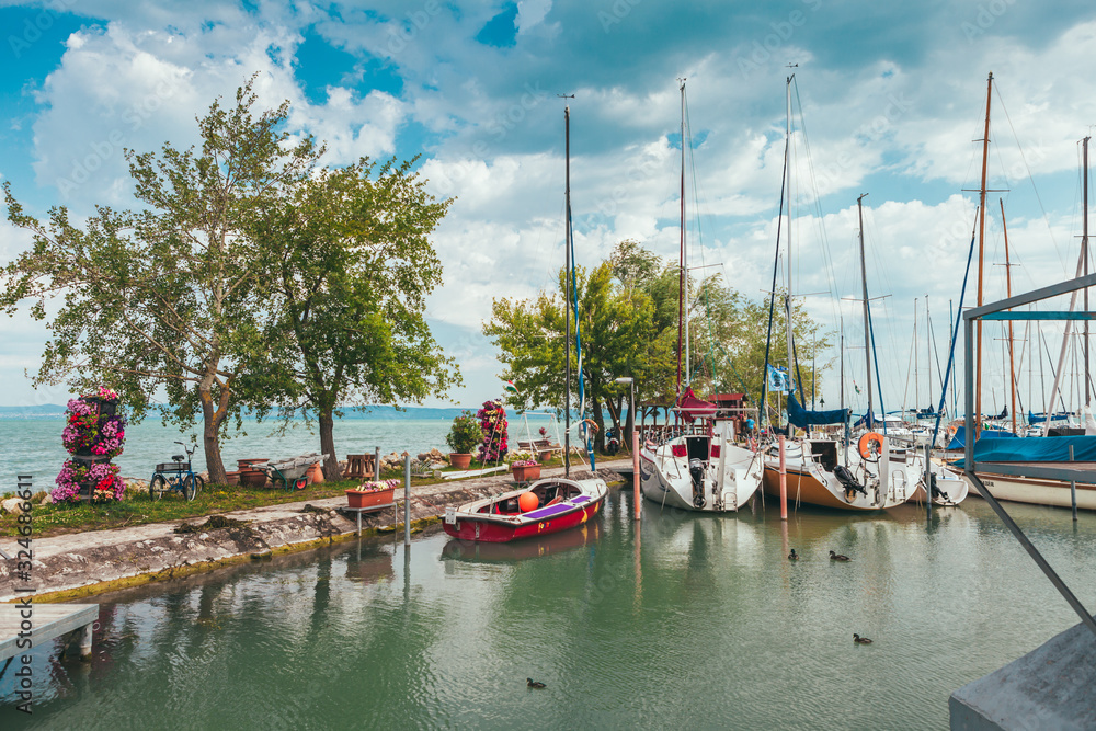 View to entrance to Siofok harbor at Balaton lake, Hungary, with crystal clear water of emerald color, green coastline, puffy clouds on sky
