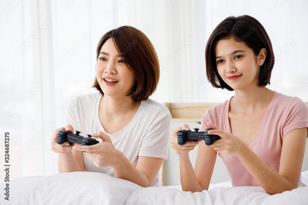 Two Asian girl hold game controller and enjoy video game together on bed. Concept for teenage or friends activity, lifestyle at home. Two Asian girl hold game controller and enjoy video game together on bed. Concept for teenage or friends activity, lifestyle at home.