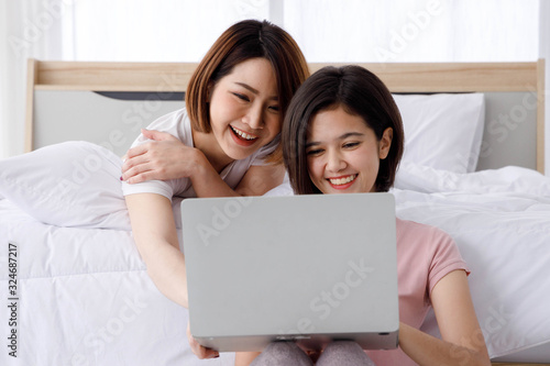 Two Happy Asian women smile and look at laptop in bright bedroom. Concept  for teenage or friends activity, lifestyle at home.