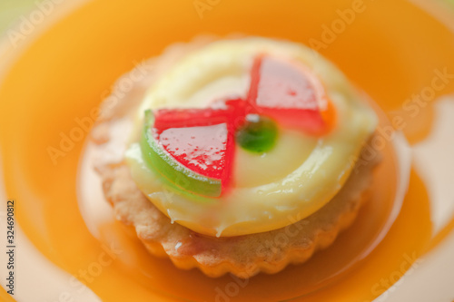 Sweet round cake with yellow cream and red jelly watermelon slices in orange plate.