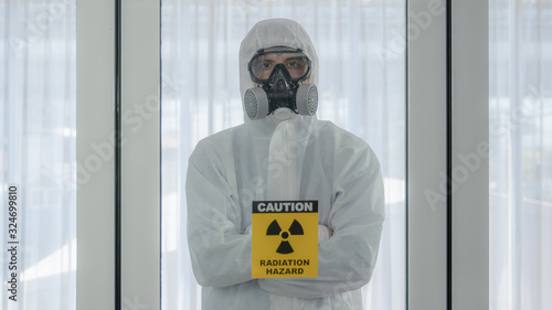 scientist with coverall protection clothing and full face protection mask in control room with radiation hazard sign