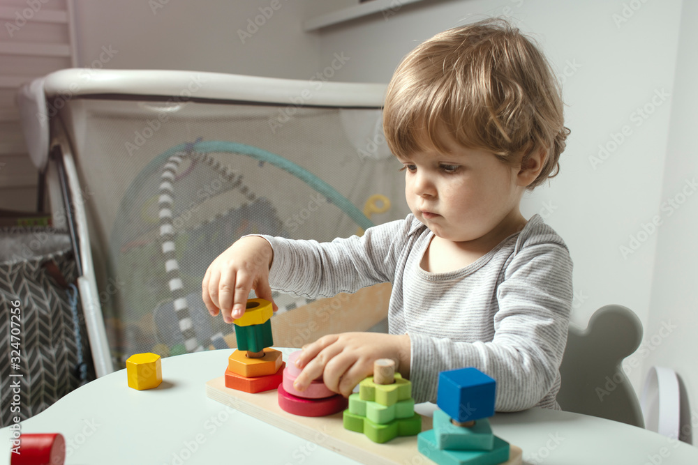 Beautiful toddler play with a wooden toys at home. Toddler play with a color educational toy. Child play at the table in the baby room. Child development. Funny baby. Lifestyle. Beautiful toddler play with a wooden toys at home. Toddler play with a color educational toy. Child play at the table in the baby room. Child development. Funny baby. Lifestyle.