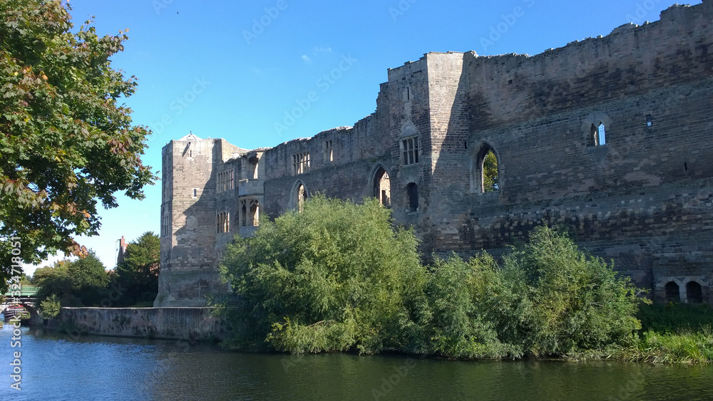 A view of the ruined walls of Newark castle seen from across the River Trent under a bright blue sky