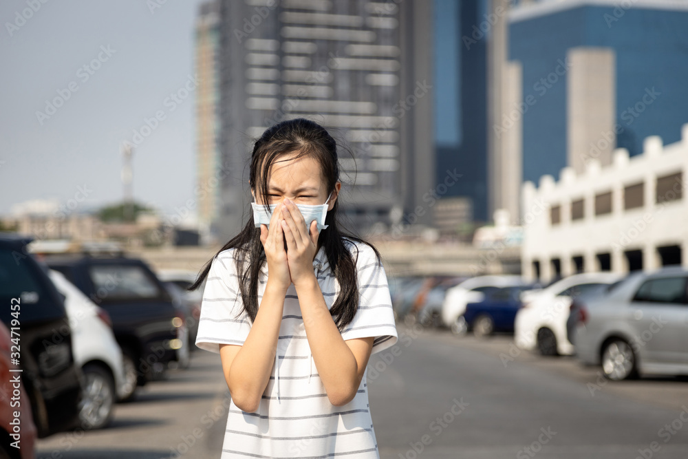 Sick asian child girl cough,sneeze wearing protective mask have severe allergic reaction to dust,air pollution,smog,polluted environment from cars in the city,contaminated air,world pollution crisis Sick asian child girl cough,sneeze wearing protective mask have severe allergic reaction to dust,air pollution,smog,polluted environment from cars in the city,contaminated air,world pollution crisis