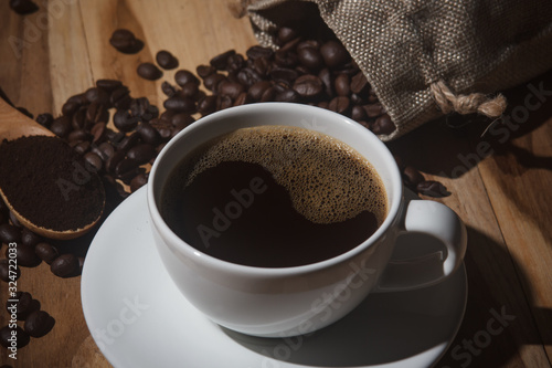 Black coffee in a white mug on a wooden table with roasted coffee beans and a spoon