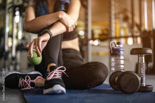 Fototapeta Naklejka Na Ścianę i Meble -  Woman sitting holding an apple after a workout in the gym at sunset. fitness ,workout, gym exercise ,lifestyle  and healthy concept.