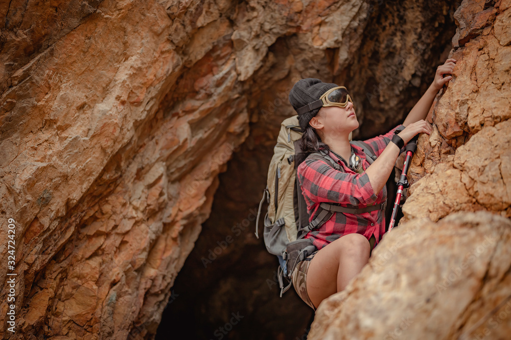 Side view of woman hiker climbing on the cliff at cave in sunset. Woman, hiking, hikers, mountain, cave, activity concept.
