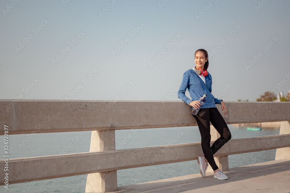 Young woman drink water and stand to rest after jogging a morning workout in the city. A city that lives healthy in the capital. Exercise, fitness, jogging, running, lifestyle, healthy concept.