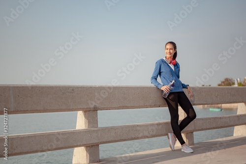 Young woman drink water and stand to rest after jogging a morning workout in the city. A city that lives healthy in the capital. Exercise, fitness, jogging, running, lifestyle, healthy concept.