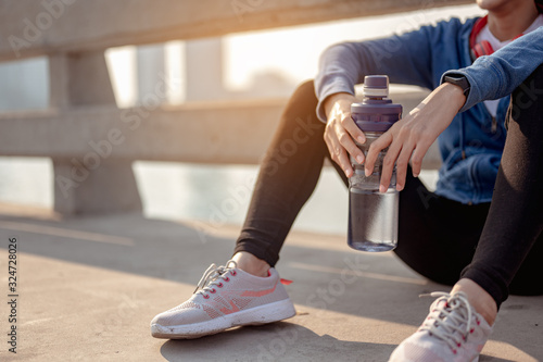 Young woman drink water and sitting to rest after jogging a morning workout in the city. A city that lives healthy in the capital. Exercise, fitness, jogging, running, lifestyle, healthy concept.