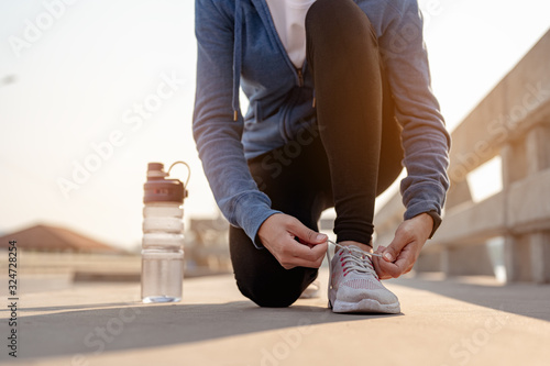 Young women using their hands to tie their shoes jogging in morning workout at the city. A city that lives healthy in the capital. Exercise  fitness  jogging  running  lifestyle  healthy concept..