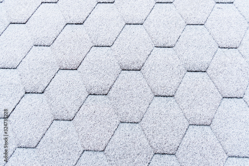 Asphalt roofing shingles texture covered with light snow. House roof shingles covered with frost. Snow covered roof of the house.