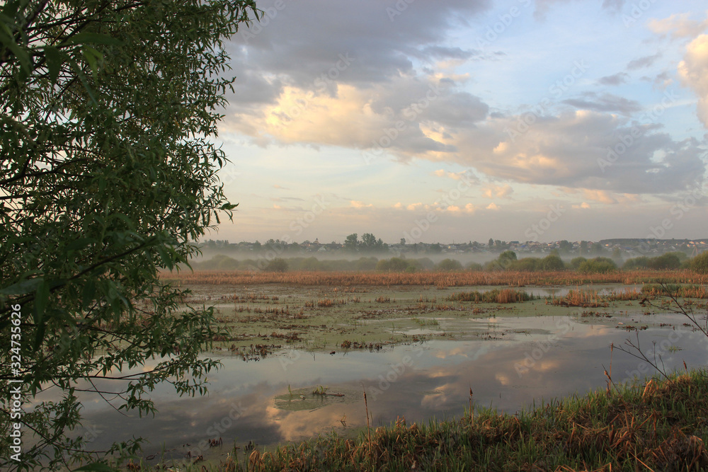 Swamp flooded with spring waters in the morning. Clouds are reflected in the water. A village in the distance.