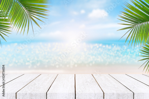 Top of wood table with seascape and palm leaves, blur bokeh light of calm sea and sky at tropical beach background.blurred blue sky and sea with bokeh light and old wooden table background