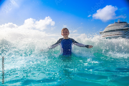 Happy Boy playing in the ocean waves while on a Cruise vacation. Aqua blue Caribbean sea water splashing the boy from behind on a warm day in the islands. © Brocreative