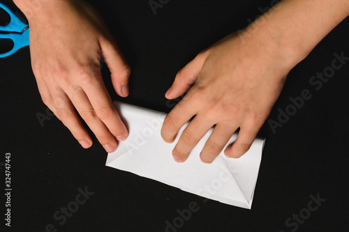 A boy on a black desk works with white paper.