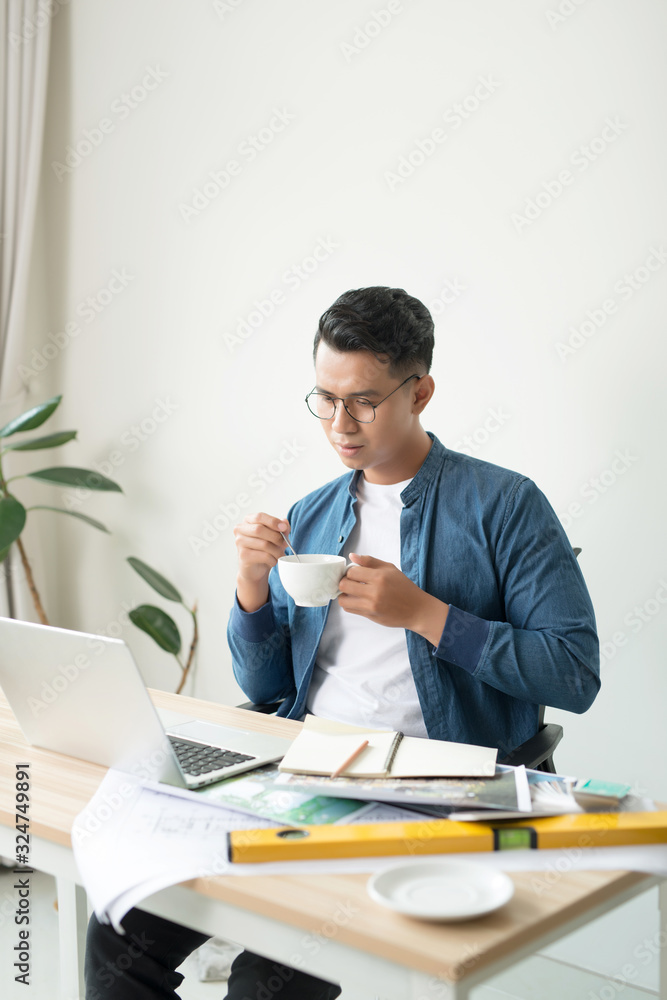 Handsome young man drinking coffee and working at his desk at the office Handsome young man drinking coffee and working at his desk at the office
