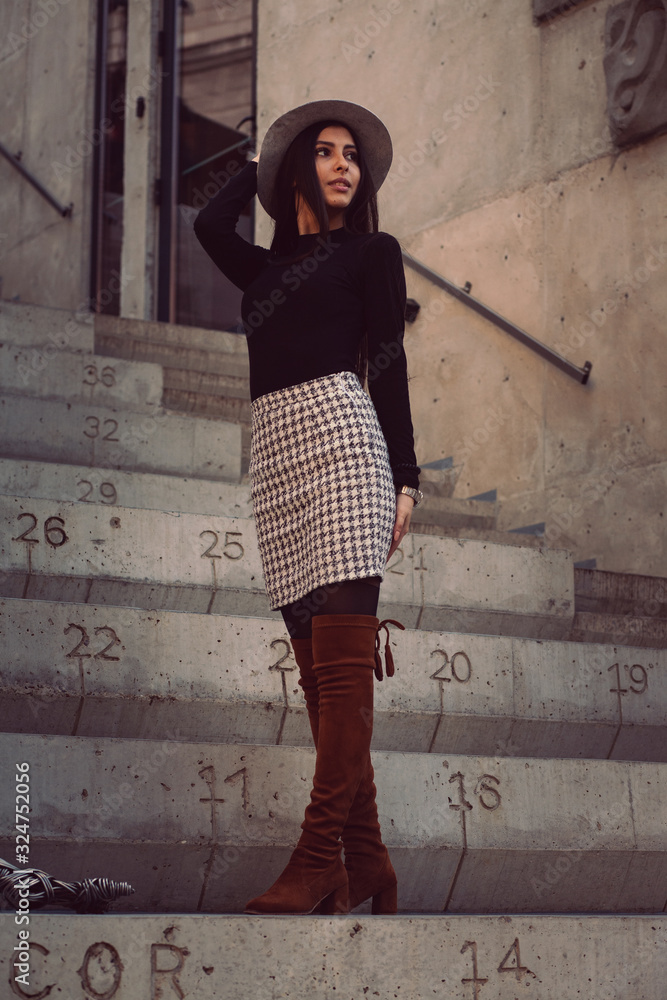 stylish girl in a hat with long hair posing on the steps of the building