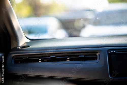 Close up of plastic car air ventilation grills from air condition system in a compact car. Selective focus points. Seeing a front glass windshield with cars parked in a parking lot in the morning.