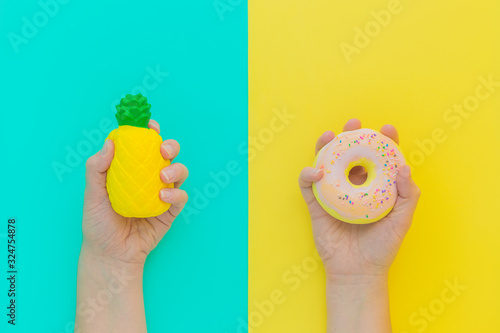 Flat lay antistress squish toys yellow pineapple,pink donut with sprinkles in hands.Bright blue background.Compressing,soft,squeezable items to relieve stress,problem,anxieties,worries.Summer concept