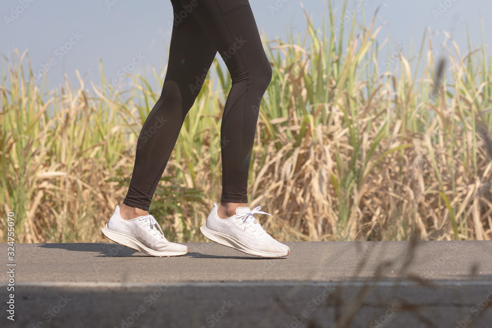 Close up Athlete running woman wearing Exercise pants and running shoe on the road,Runner woman traning in the morning.Walking for warm up her muscle. Close up Athlete running woman wearing Exercise pants and running shoe on the road,Runner woman traning in the morning.Walking for warm up her muscle.
