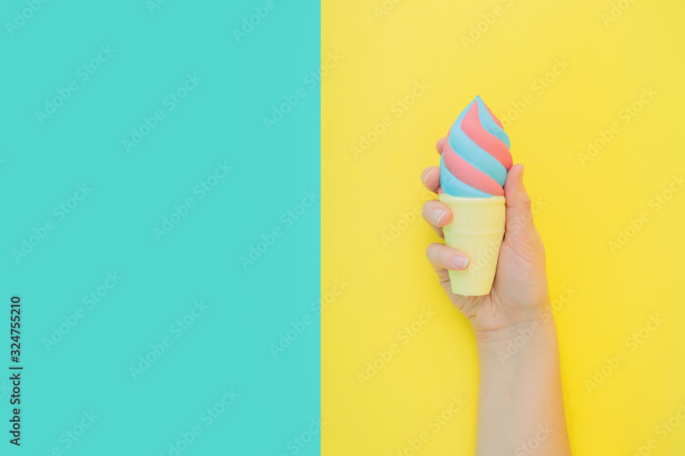 Flat lay antistress toy squish ice cream in waffle cone squezzed in hand.Bright blue yellow background.Compressing,soft,squeezable items to relieve stress,problems,anxieties,worries.Summer concept