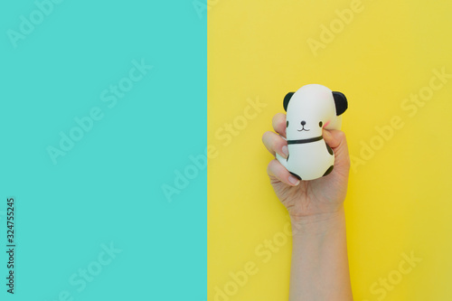 Flat lay antistress toy squish black white big panda squeezed in hand.Bright yellow blue background.Compressing, soft, squeezable items to relieve stress, problems, anxieties, worries.Summer concept