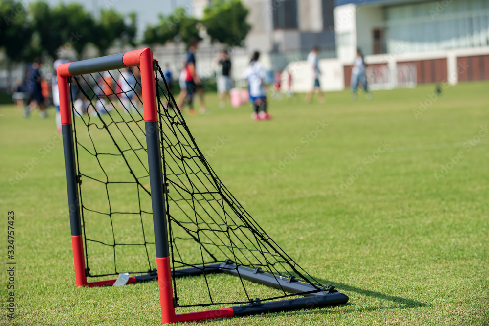 A small size of black and red plastic goal with black net for junior football teams placed on a school tournament pitch. Seeing groups of players and parents walking around in a background.