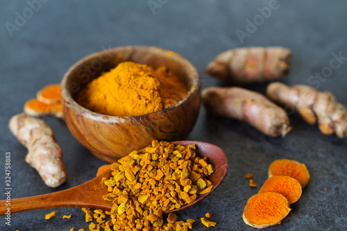 Turmeric powder and turmeric roots and slices on dark background