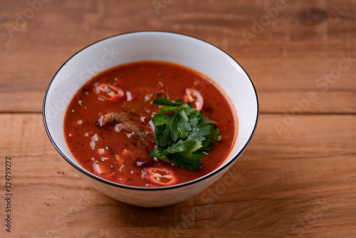Traditional Ukrainian Russian vegetable borscht in a white bowl on the old rustic wooden background.