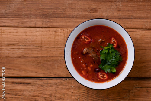 Traditional Ukrainian Russian vegetable borscht in a white bowl on the old rustic wooden background. Copy space.