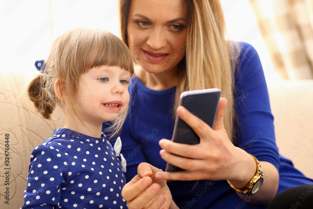Cute little girl on floor carpet with mom use cellphone calling dad portrait. Life style apps social web network wireless ip telephony concept Cute little girl on floor carpet with mom use cellphone calling dad portrait. Life style apps social web network wireless ip telephony concept