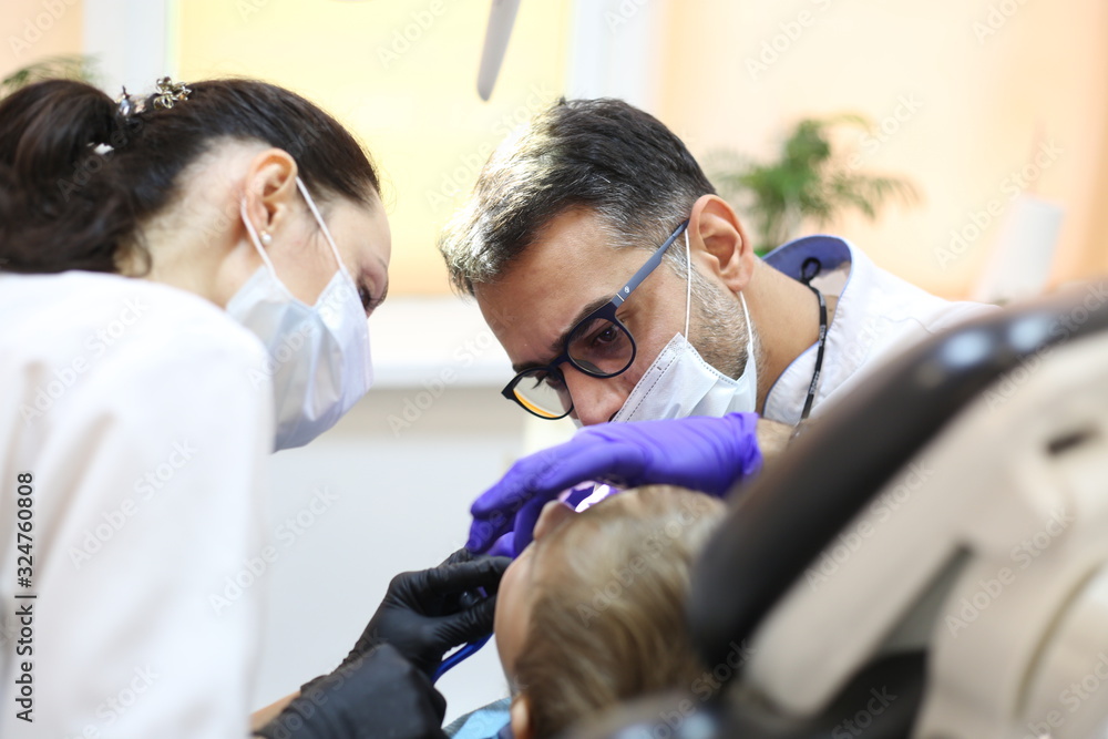 dentist is diagnosing the child while assistant in dental clinic dentist is diagnosing the child while assistant in dental clinic