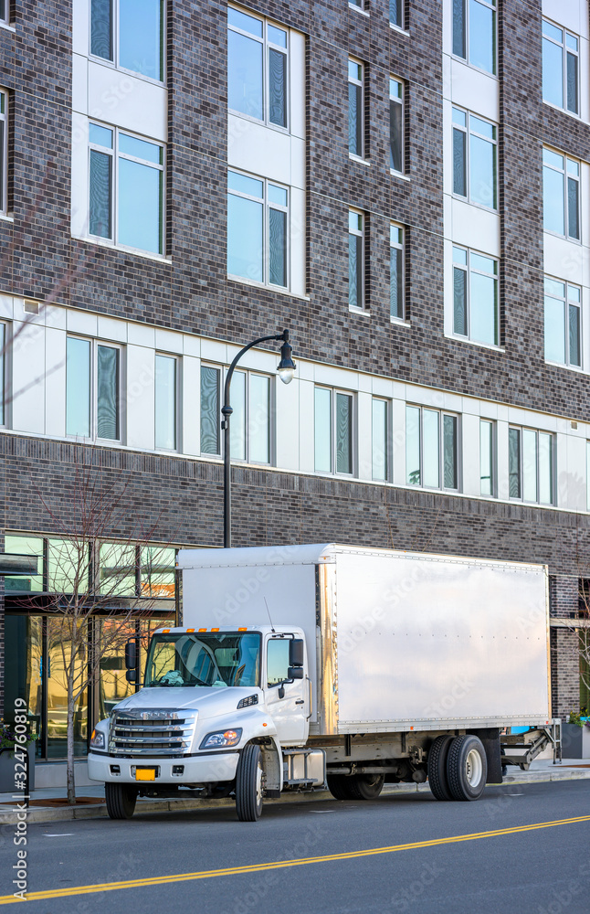 Medium power compact rig semi truck with box trailer delivered goods to multilevel apartments building on the urban city street