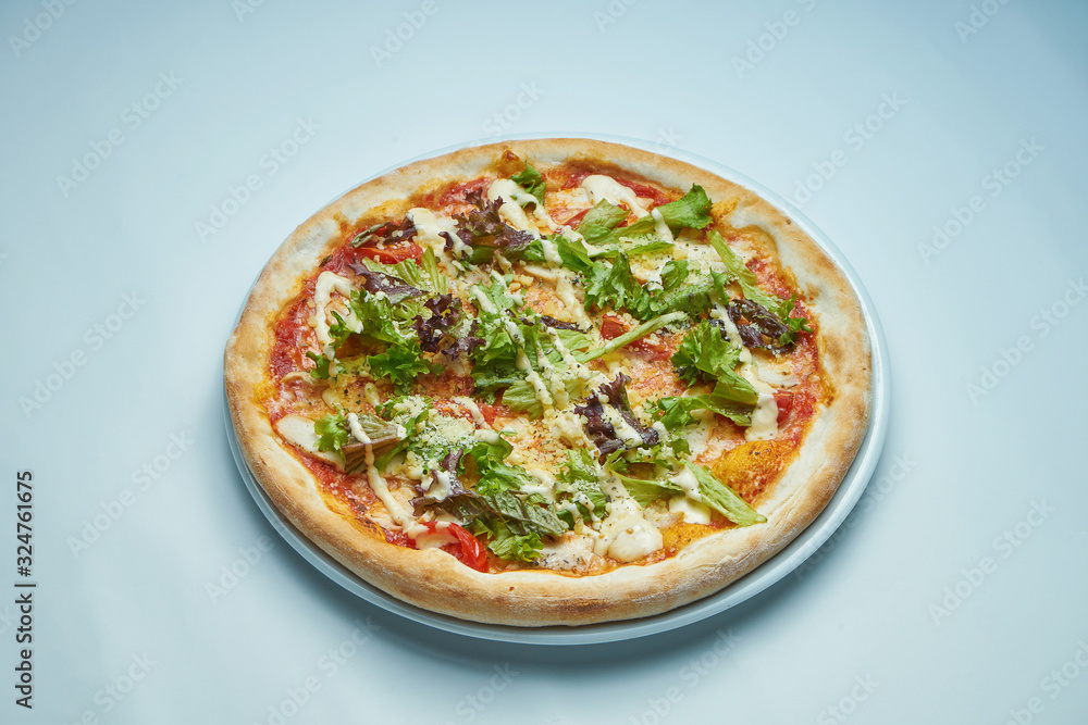Appetizing baked Italian pizza with cream sauce, lettuce, chicken and parmesan on a white plate on a gray background. Pizza caesar