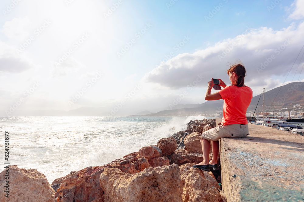Attractive mature traveler woman use mobile phone take a photo of beautiful seascape. Attractive mature traveler woman use mobile phone take a photo of beautiful seascape.
