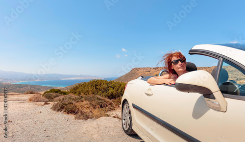 Happy Mature woman with sunglasses in convertible top automobile on mountain road.