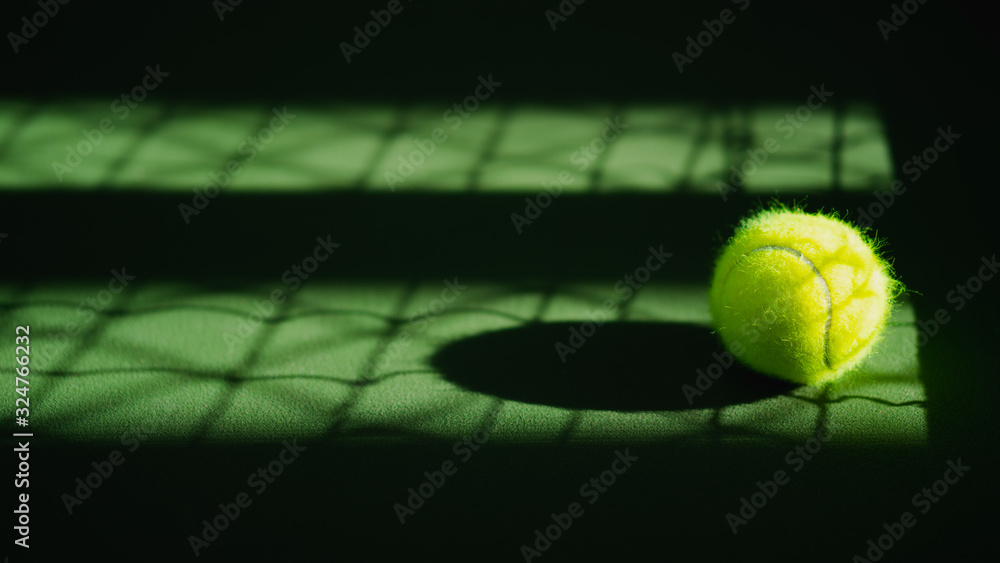 one new tennis ball and net shadow on green hard court with light from right, copy space on left