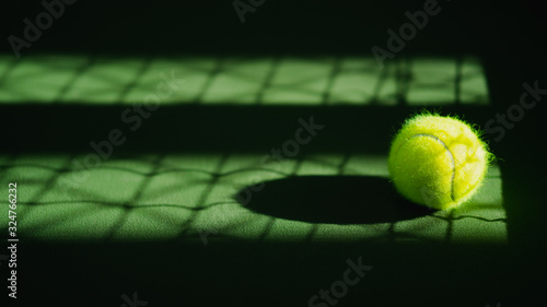 one new tennis ball and net shadow on green hard court with light from right, copy space on left © angyim